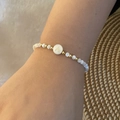 Close-up of beaded bracelet featuring white beads and a golden letter A charm on a wrist - Letter A Style (A)