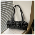 Dettaglio di una borsa a cilindro nera con eleganti fiocchi appoggiata su un libro - Nero