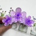 Three purple flower hair clips in various sizes held by hand for elegant hair styling - Purple