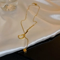 Detalle de un collar de titanio dorado con colgante de letra D y cubo sobre satén blanco - Collar Letra D Dorado