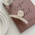 Detailed view of cream acetate shark clip with gold logo on a vintage book - Pearl White
