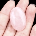 Handheld view of an oval pink rose quartz gemstone showing natural textures and polished finish - Rose Quartz