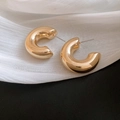 Detailed view of chunky golden C-shaped hoop earrings on elegant white draped fabric - Gold Wide Chunky C-Shape
