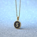 Golden coin necklace with black enamel pendant and letter S on a bokeh background - Letter S