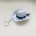 Detailed close-up of a white felt mini cowboy hat keychain with a blue band and star stud - White
