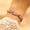 Dettaglio di un bracciale dorato con cristalli viola quadrati e strass scintillanti - Viola