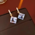 Macro view of gold sparkling diamond earrings on premium brown leather jewelry box - Square Zirconia Style / Gold