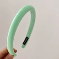 Detail of mint green padded sponge headband with black handmade label held by hand - Green