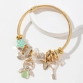 Golden twisted rope bangle with heart crown, key, and love charms on a white platform - Green