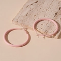 Nahaufnahme rosa mattierter Creolen auf Steindisplay mit minimalistischer Ästhetik - Rosa