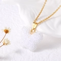 Gros plan d'un collier pendentif papillon blanc givré sur une chaîne dorée - Blanc