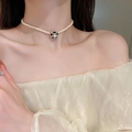Dettaglio collana di perle con ciondolo a camelia indossata sul collo di una donna - Perla Camelia (31#) / Nero