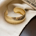 Close-up of golden wide cuff bracelet with vintage floral relief on textured linen fabric - Gold