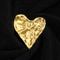 Macro shot of irregular hammered gold heart brooch on shimmering black fabric - Gold
