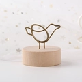 Bird-shaped metal wire photo clip with cylindrical wood base on white mesh background - Bird