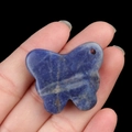 Deep blue natural stone butterfly pendant with white veins held against black background - Blue Sodalite