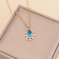 Detailed close-up of a pear-shaped blue gemstone pendant on a gold twisted chain necklace - Lake Blue