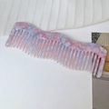 Macro detail of wave-shaped marble texture acetate wide-tooth hair comb on fabric - Pink Purple