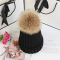 Flat lay of a black knit beanie with a khaki faux fur pom pom in a gift-style setting - Adult One Size 56-58cm / Black