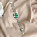 Detail of square green dial watch with silver mesh strap on warm fabric background - Silver Case Green Dial