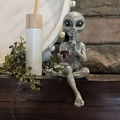 Grey resin alien statue sitting on wood holding a wine glass and making a shush gesture - Grey Alien with Red Wine