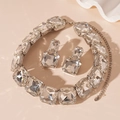Detalle de conjunto de joyas de plata con cristales cuadrados sobre fondo rosa claro - Juego de Collar y Pendientes Cuadrados de Strass Plateado