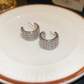 Close-up of silver C-shaped hoop earrings with pave cubic zirconia on a ceramic tray - Silver