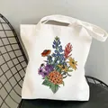 White canvas tote bag with colorful wildflower floral illustration on a black chair - C6 Lupine and Hydrangea