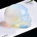 Handcarved opalite crystal skull with blue and yellow iridescent glow on white card - Opalite Skull-1.5 Inches