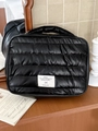 Close-up of black quilted puff makeup bag with textile label on wooden surface - Black