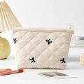 Detailed close-up of quilted cosmetic bag with black bow embroidery on cream fabric - Beige