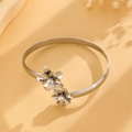 Dettaglio di un bracciale rigido a fiori argentati con cristalli lucidi su sfondo beige - Bracciale Aperto a Doppia Fioritura Argento (0994)