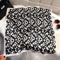 Elegant silk square scarf with black and white geometric patterns on a soft white rug - Black