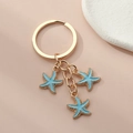 Gros plan d'un porte-clés doré orné de trois étoiles de mer en émail bleu clair sur fond rose - Étoile de mer / Bleu clair