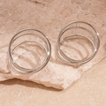 Vista detallada de anillos plateados de tres capas sobre fondo de piedra beige - Plateado