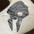 Detalle de bufanda triangular de punto gris con etiqueta sobre fondo de gofre suave - Gris claro
