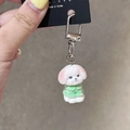 Dettaglio di un portachiavi a forma di cane Bichon bianco con maglione verde e gancio - Cane