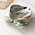 Close-up of paisley pattern fabric headband with bow detail and satin trim - Green