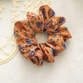 Dettaglio di uno scrunchie arancione con motivo a rose su sfondo di pizzo decorativo - Arancione