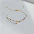 Detail eines verstellbaren Perlenarmbands mit goldenem T-Anhänger im Boho-Stil - Buchstabe T