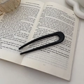 Forcina per capelli nera a forma di U con finitura liscia posata su un libro aperto - Nero
