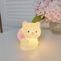 Cartoon bear night light in warm yellow glow, cute glowing animal toy on white table - Tulip Bear
