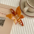 Detailed view of amber butterfly hair claw clip with lifestyle magazine and coffee props - Caramel color