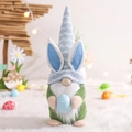 Detalle de un gnomo de Pascua con orejas de conejo sosteniendo un huevo azul decorativo - Estilo Hombre Con Huevo Azul