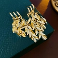 Close-up of golden leaf tassel earrings on a textured gift box showing fine metal details - Gold