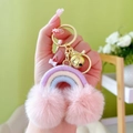 Bohemian rainbow keychain with macaron pompoms and gold metal clasp in hand - Purple Pink