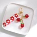 Detail of red cherry pendant with golden clasp and floral embroidery strap keychain - Apple