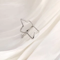 Macro view of a silver star-shaped open ring on white silk, showing polished metal texture - Silver Tone Star Outline