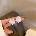 Detailaufnahme von weißen Blumen-Ohrringen mit Perlen und Quasten in der Hand - Weiß