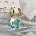 Detail der goldenen Delphin-Ohrringe mit hellblauen Steinen auf Stein-Display - Delfin